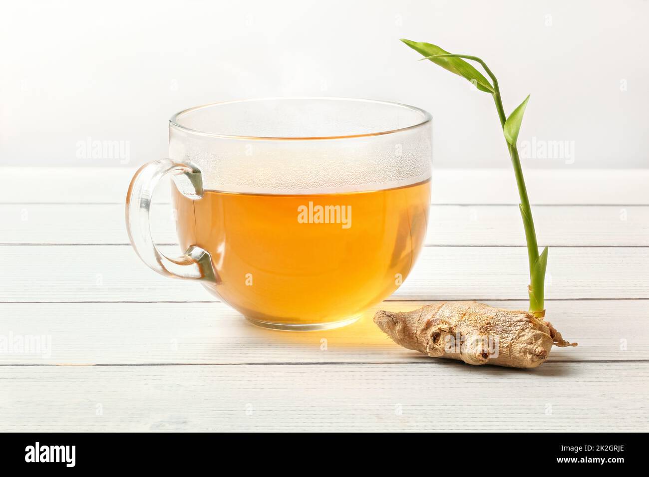 Racine de gingembre sec avec green sprout sur table en verre blanc sangliers, tasse de thé fraîchement infusé à côté. Banque D'Images