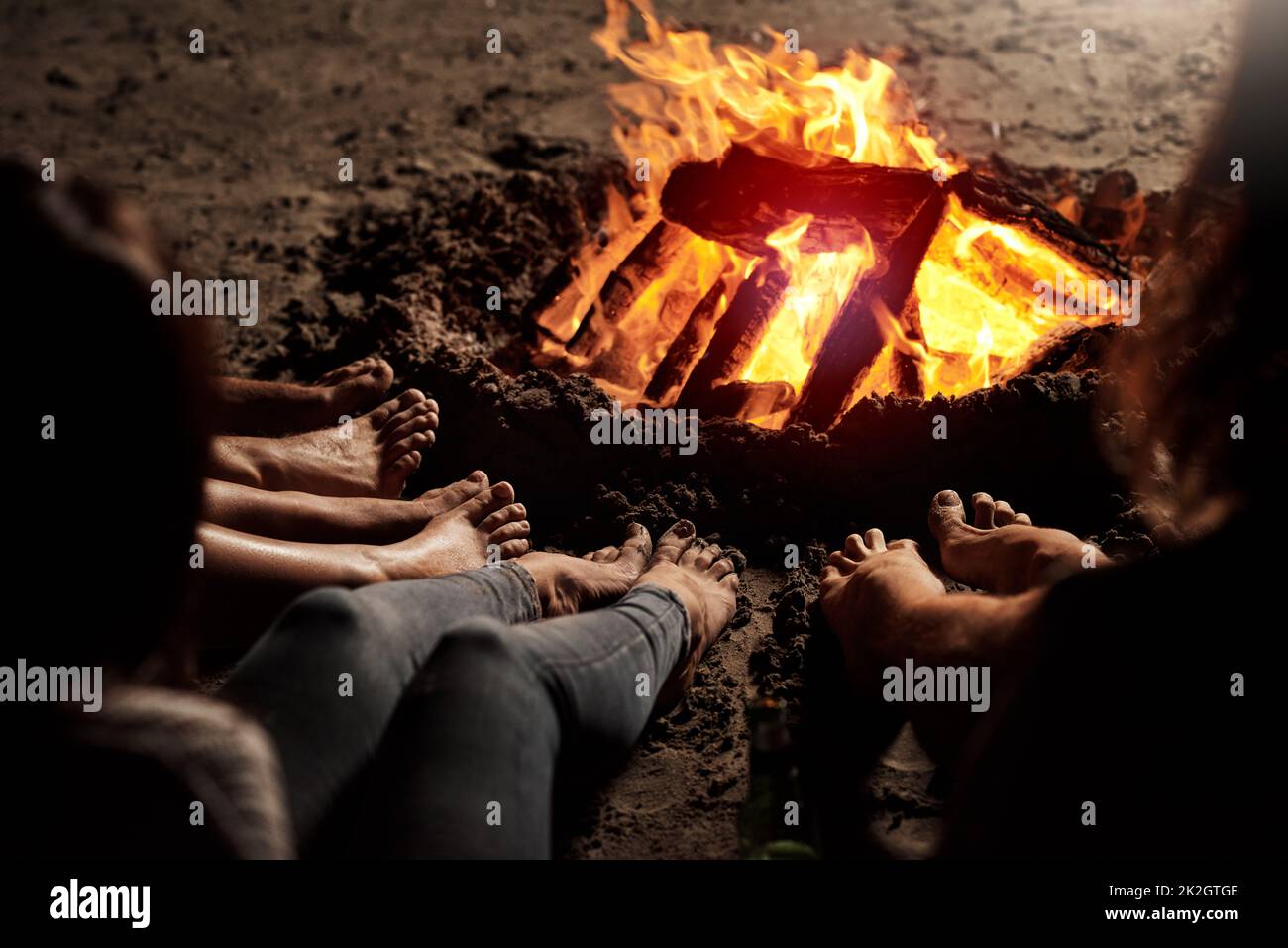 Collage par le feu de camp. Photo rognée d'un groupe d'amis méconnaissables assis autour d'un feu de camp sur la plage la nuit. Banque D'Images