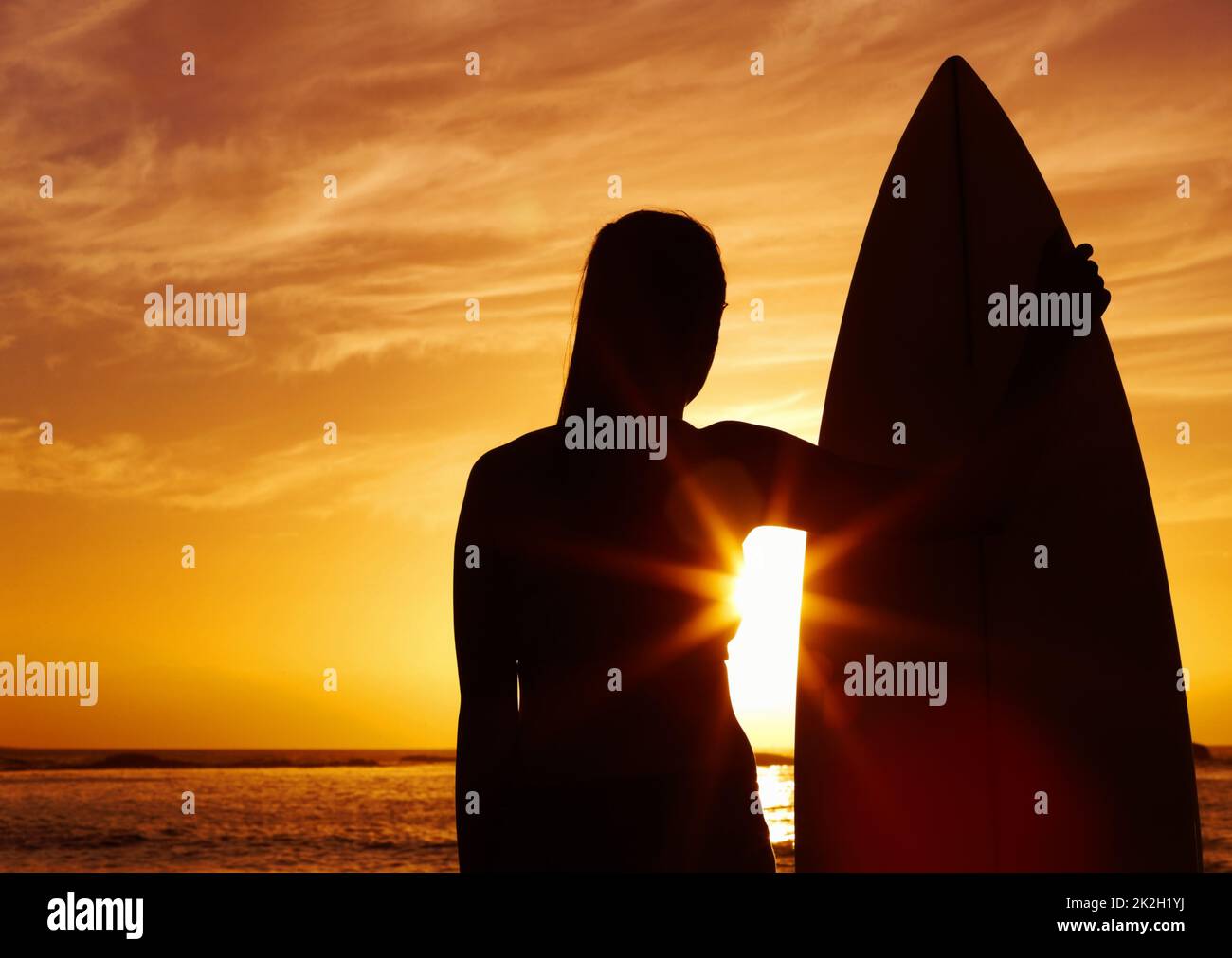 Silhouette d'une femme tenant une planche de surf au coucher du soleil. Silhouette d'une belle femme tenant une planche de surf au coucher du soleil. Banque D'Images