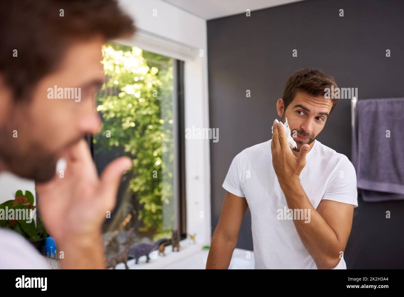 Crème de rasage d'abord pour protéger ma peau. Coupe courte d'un beau homme appliquant de la crème à raser sur son visage dans la salle de bains à la maison. Banque D'Images