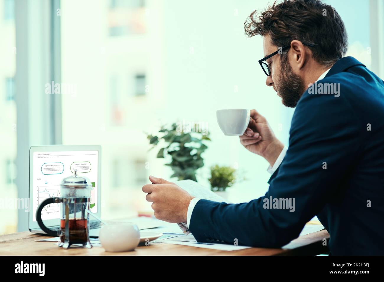 Il commence la journée avec un cuppa et le papier. Photo d'un jeune homme d'affaires qui boit une tasse de thé tout en lisant un journal dans un bureau. Banque D'Images
