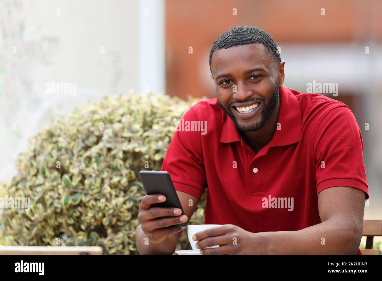 Un homme heureux avec une peau noire regarde l'appareil photo avec un téléphone Banque D'Images