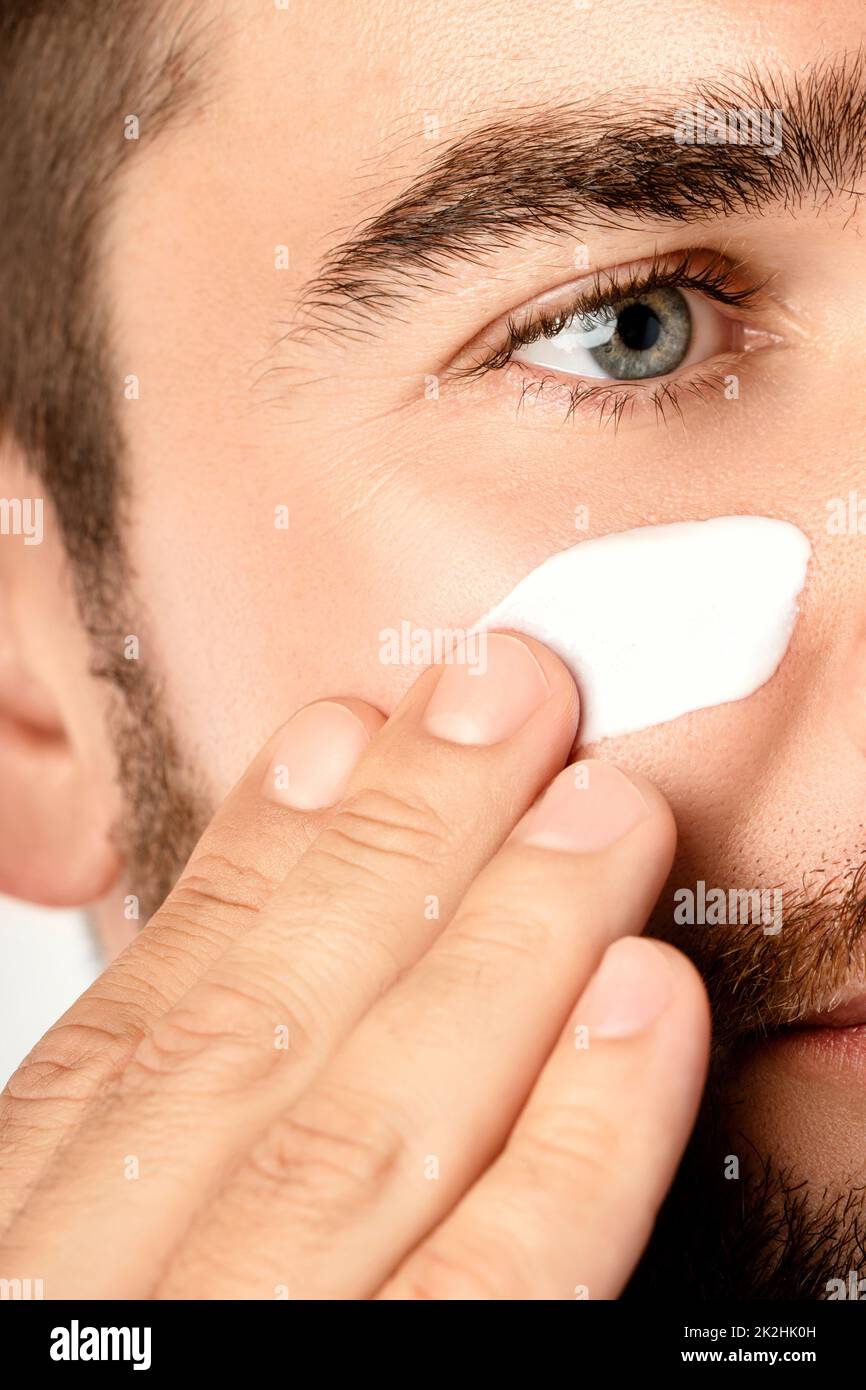 Le jeune homme applique de la crème hydratante et anti-âge sur son visage Banque D'Images