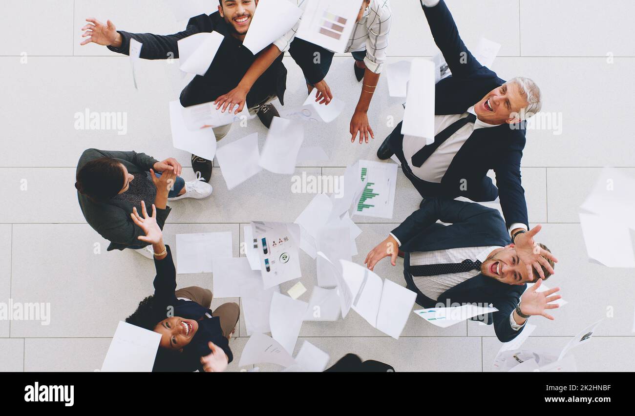 Prise de vue aérienne d'un groupe diversifié d'hommes d'affaires qui jettent des documents dans les airs lors de célébrations au bureau Banque D'Images