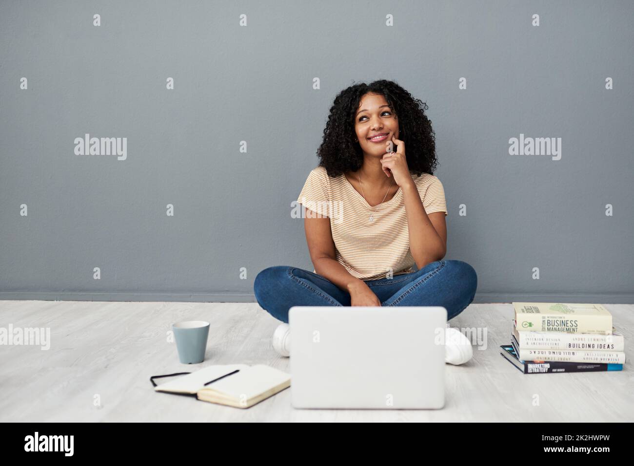 Les universités sont désormais virtuelles.Photo en studio d'une jeune femme utilisant un ordinateur portable tout en réalisant ses études sur un fond gris. Banque D'Images