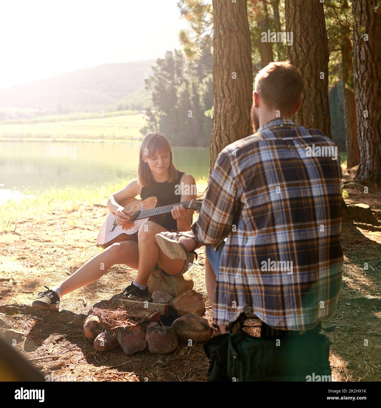 Profiter d'un voyage de camping frais.Prise de vue d'une jeune femme jouant de la guitare pour son petit ami à leur campement. Banque D'Images