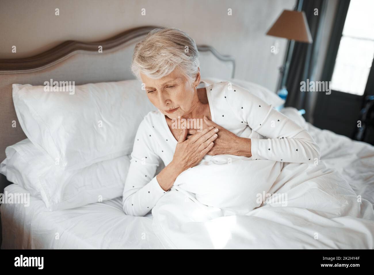Personne n'est à l'abri.Prise de vue d'une femme âgée souffrant de douleurs thoraciques au lit dans une maison de soins infirmiers. Banque D'Images