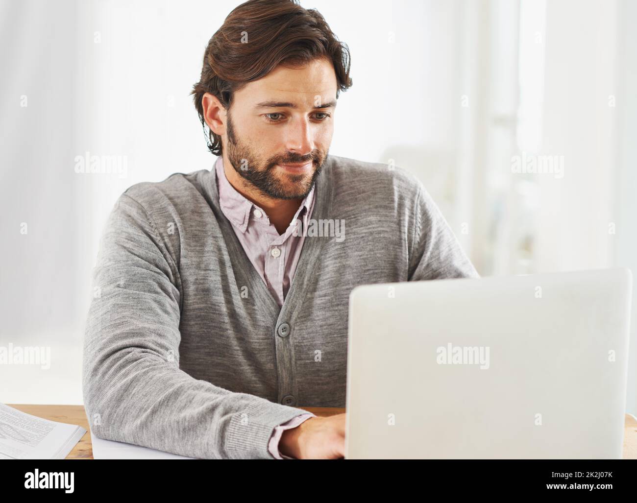 Connecté au monde.Un homme d'affaires charmant assis à son bureau et travaillant sur son ordinateur portable. Banque D'Images