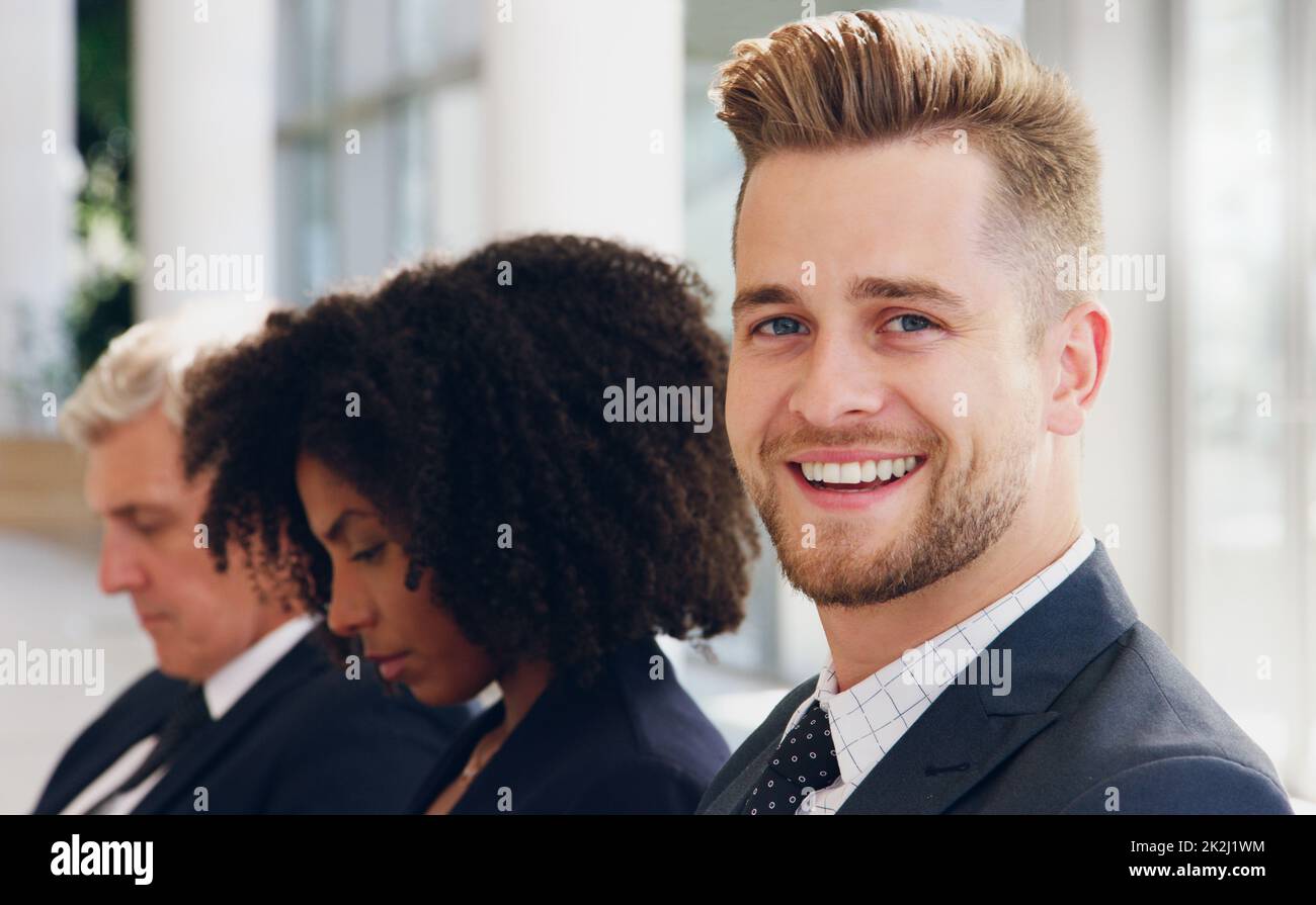 Attendre dans la file ne me dérange pas.Portrait court d'un beau jeune homme d'affaires souriant assis en ligne avec ses collègues au bureau. Banque D'Images