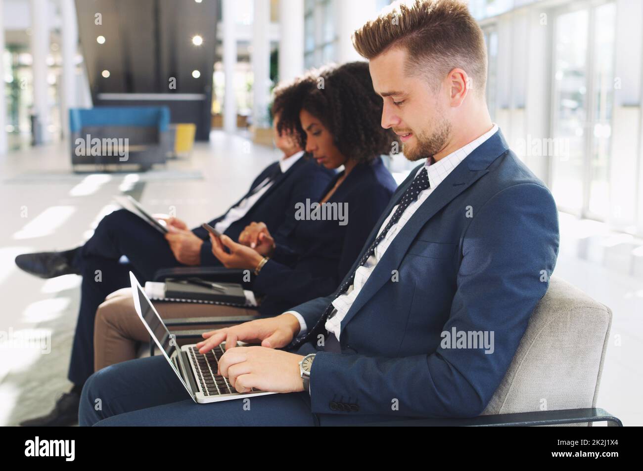 Travailler pendant que j'attends.Photo courte d'un beau jeune homme d'affaires à l'aide d'un ordinateur portable, assis en ligne avec ses collègues au bureau. Banque D'Images