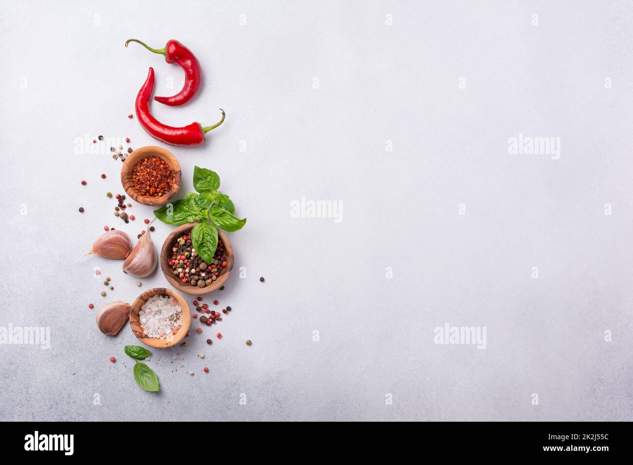 Vue de dessus du poivre, du sel, de l'ail, du basilic et du piment rouge chaud pour des aliments épicés et aromatiques sur fond de béton gris avec espace de copie Banque D'Images