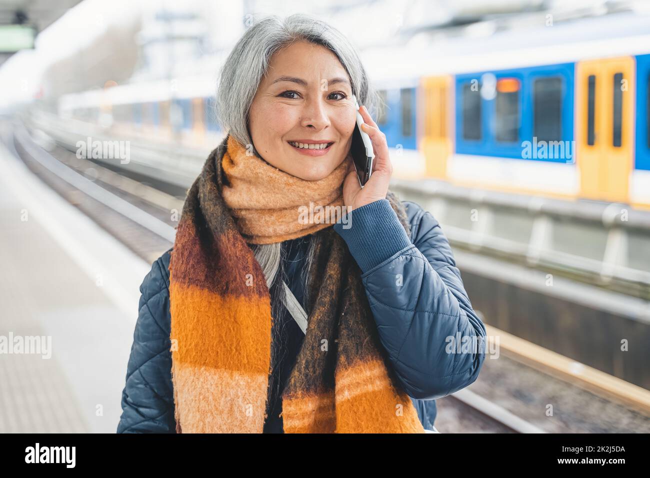 Une femme âgée envoie un message avec un téléphone portable et attend un train Banque D'Images