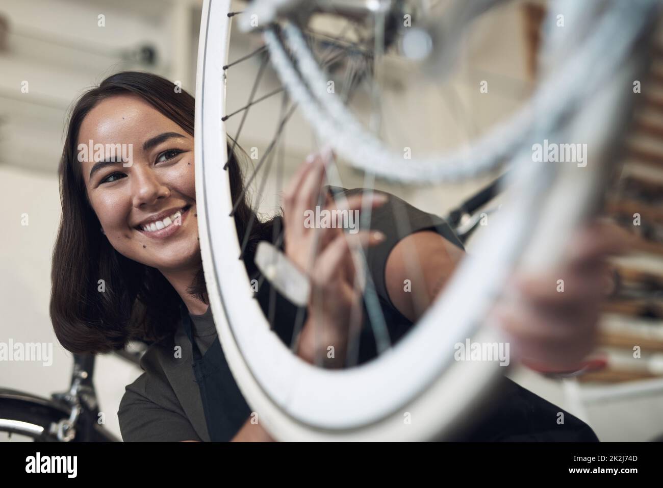 Je peux voir la vie vécue par ce vélo. Photo d'une jeune femme attirante debout seule dans son atelier et en train de réparer une roue de vélo. Banque D'Images