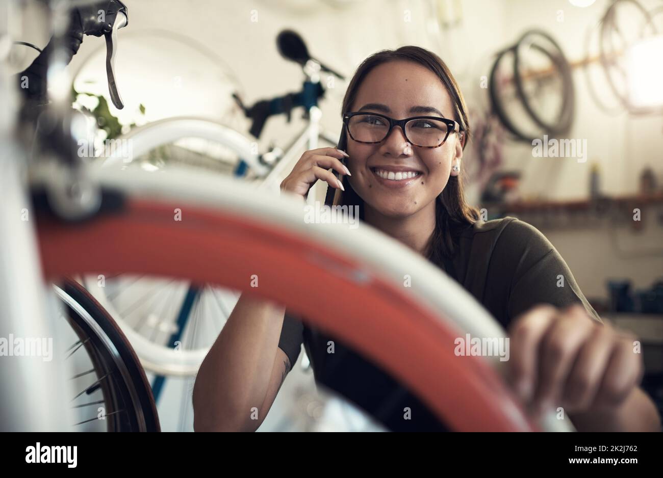 Il vous suffit d'appeler pour confirmer que nous avons bien reçu votre vélo. Prise de vue d'une jeune femme attirante qui s'est accroupie dans sa boutique de vélos et en utilisant son téléphone portable. Banque D'Images
