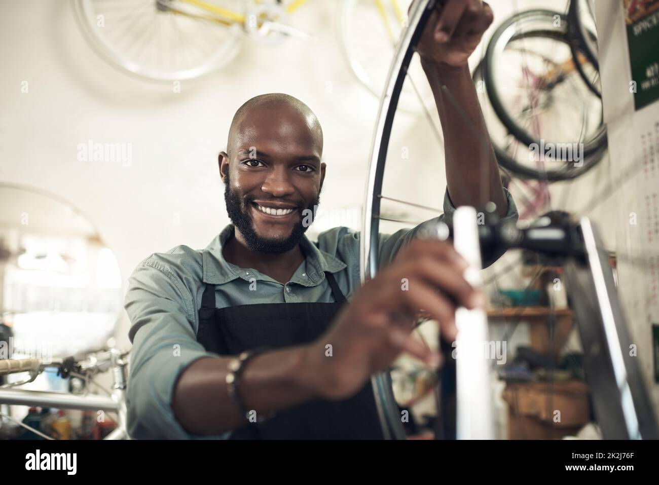 J'aime ce que je fais. Photo d'un beau jeune homme debout seul dans son atelier et réparant une roue de vélo. Banque D'Images