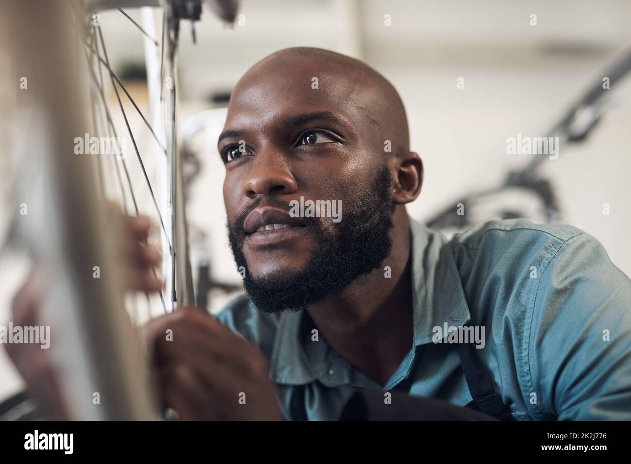 C'est encore tordu. Photo d'un beau jeune homme qui s'est accroupi dans son atelier et a réparé une roue de vélo. Banque D'Images