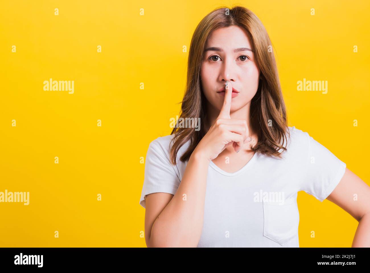 femme adolescent sourire debout porter t-shirt faire le doigt sur les lèvres silencieux geste Banque D'Images