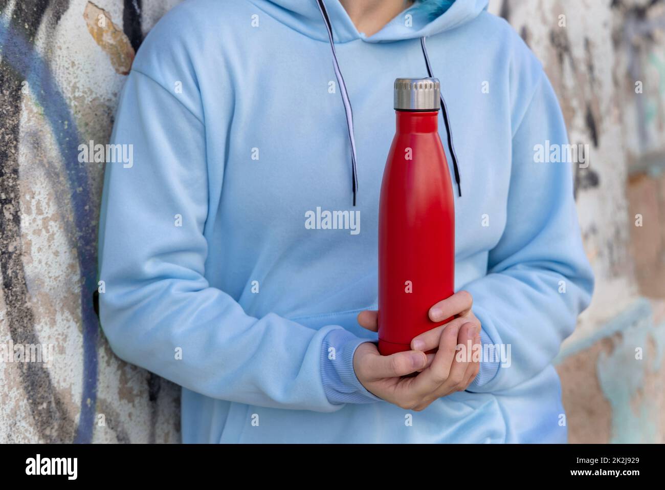 Jeune femme à capuchon bleu restant près du mur de graffiti avec une bouteille d'eau rouge Banque D'Images