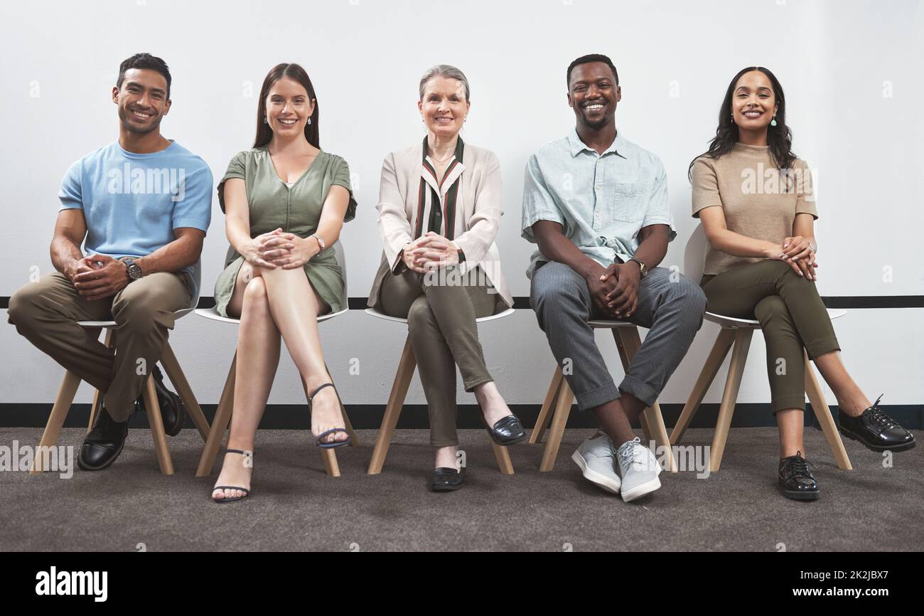 Confiant et désireux de prouver leur talent. Portrait d'un groupe de gens d'affaires assis ensemble dans une ligne contre un mur blanc. Banque D'Images