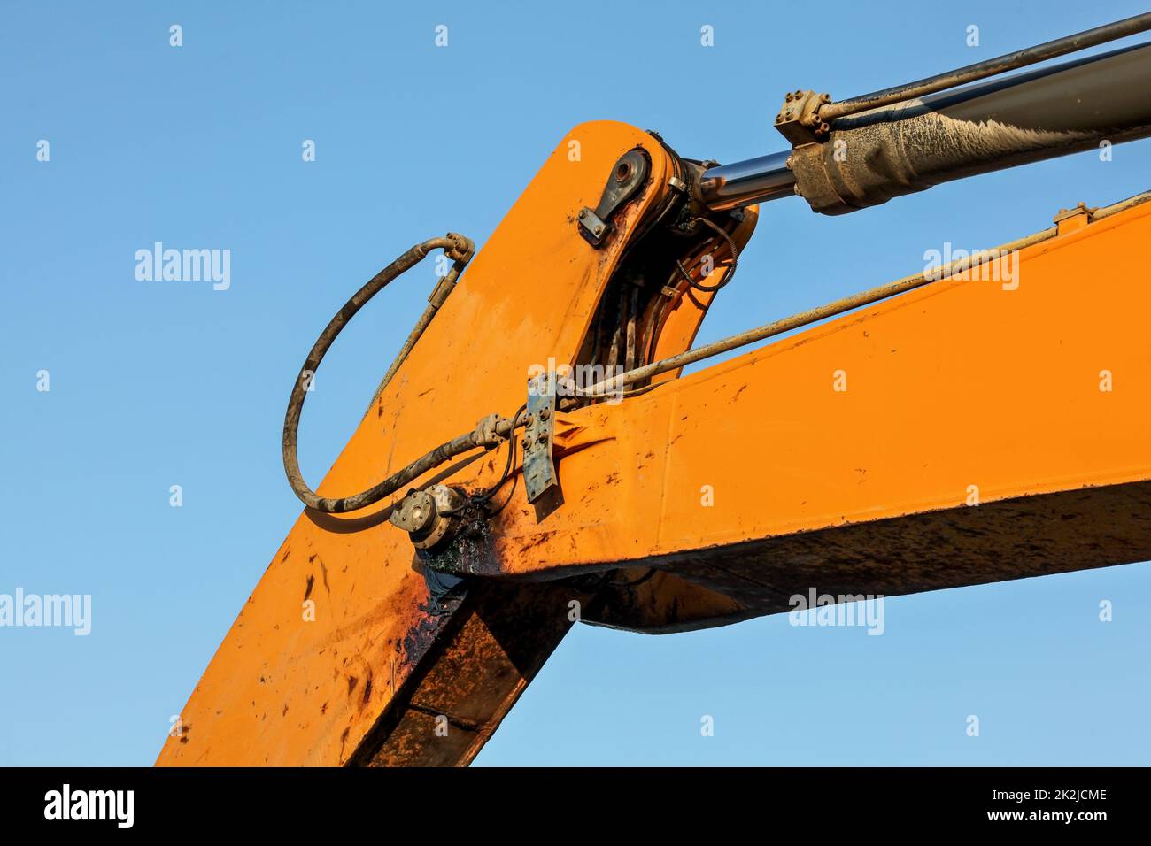 Détails sur le bras orange de la machine de pelle hydraulique, mécanisme de piston hydraulique et joint encrassés par l'huile noire visibles. Contraste bleu ciel l'après-midi en arrière-plan. Banque D'Images