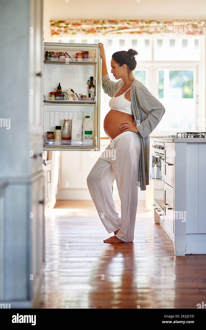Se demander quoi manger. Prise de vue d'une femme enceinte regardant à l'intérieur d'un réfrigérateur. Banque D'Images