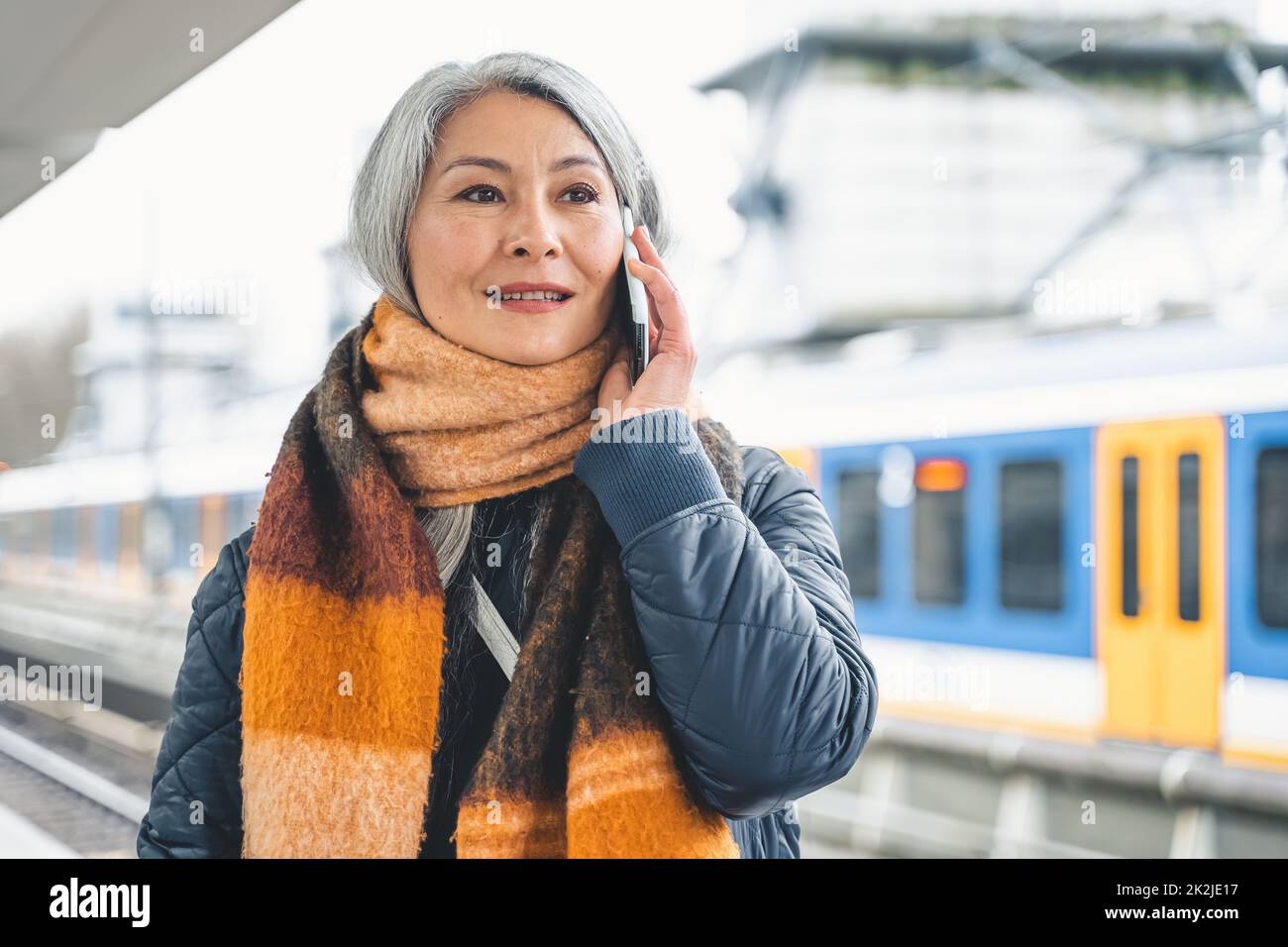 Une femme âgée envoie un message avec un téléphone portable et attend un train Banque D'Images