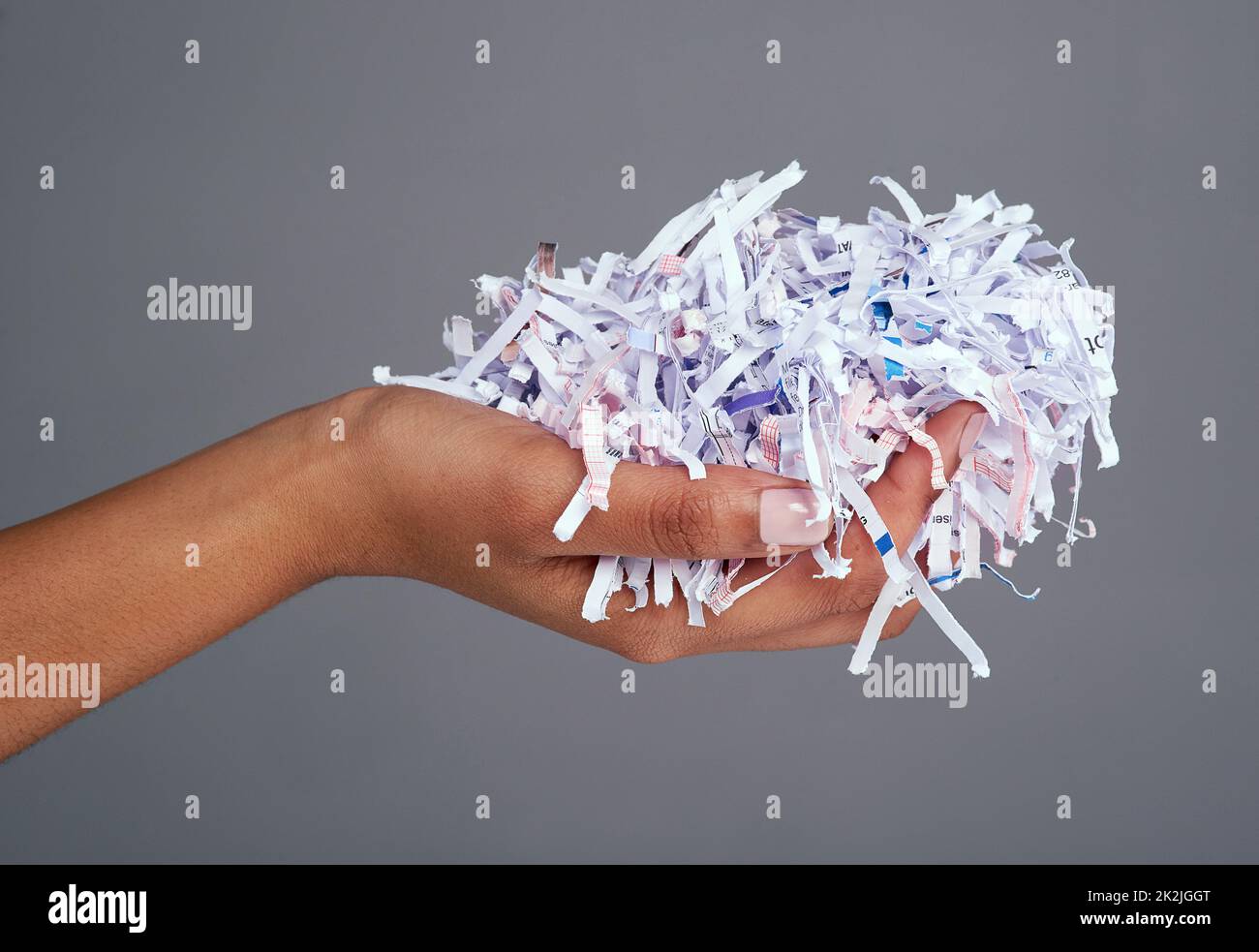 Protégez vos informations. Photo de studio d'une main de femme tenant une pile de papier déchiqueté sur un fond gris. Banque D'Images