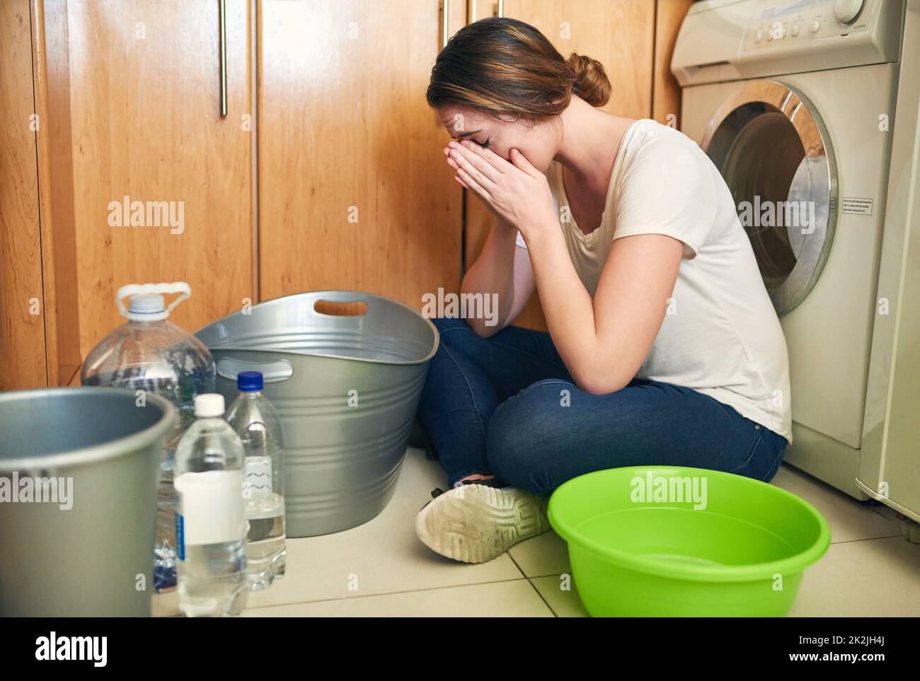 Sentiment de stress à propos de la crise de l'eau. Photo d'une belle jeune femme qui pleure sur le sol dans la cuisine à la maison. Banque D'Images