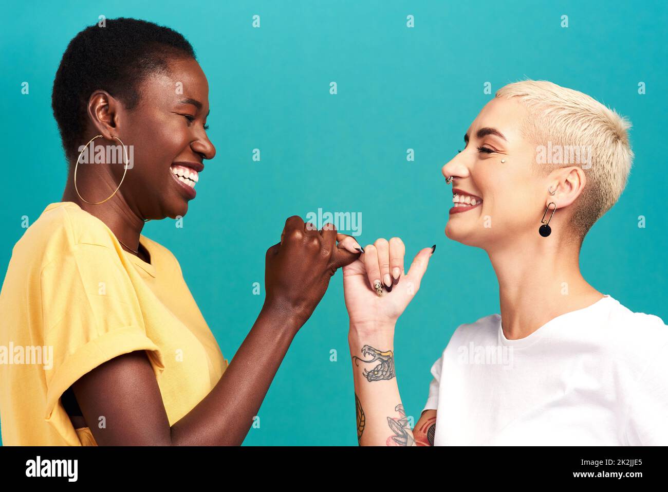 Besties pour toujours à travers tout.Studio de deux jeunes femmes reliant leurs doigts sur un fond turquoise. Banque D'Images