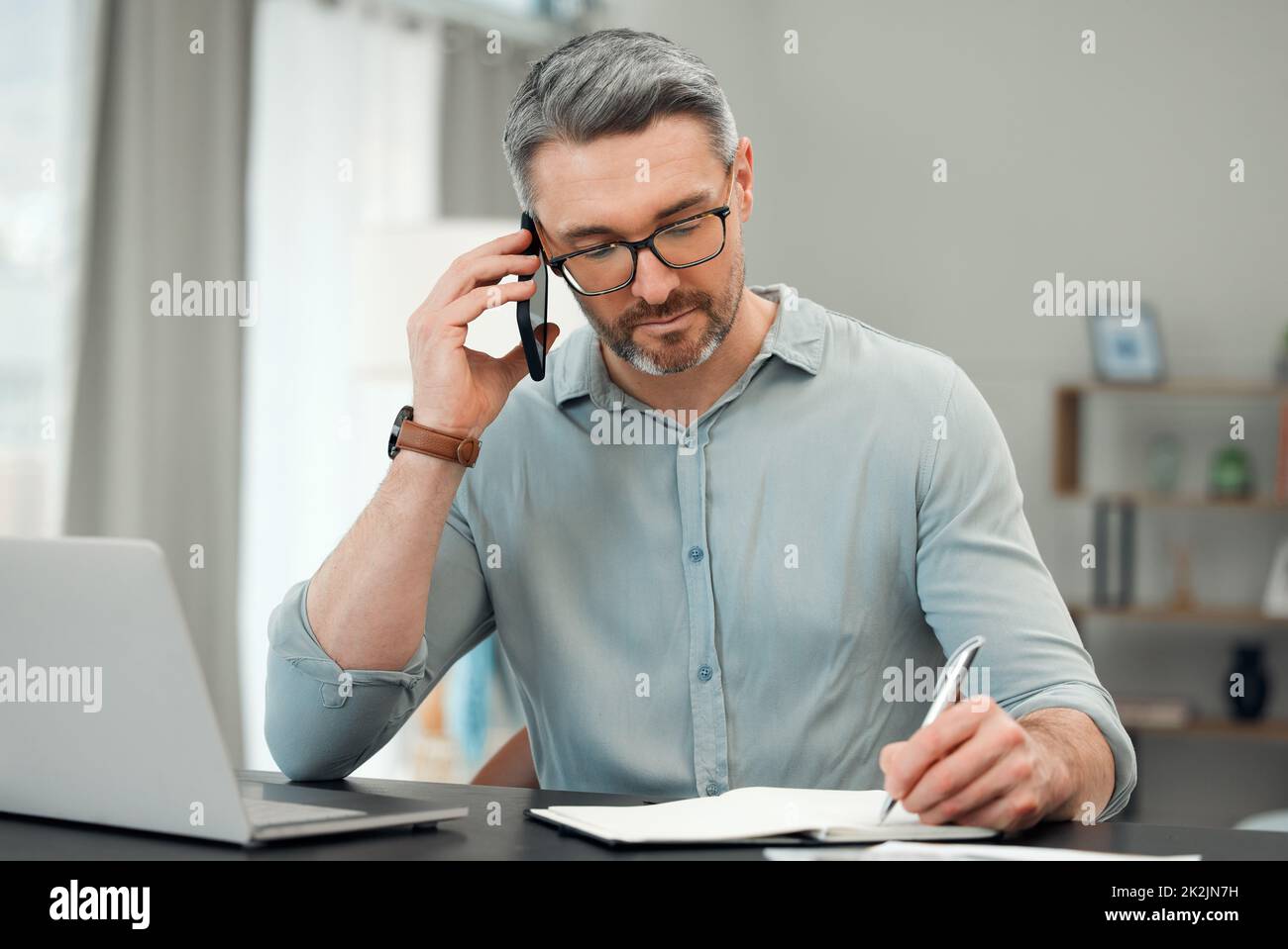 Au téléphone avec son banquier privé. Plan court d'un beau homme mûr faisant un faux-faux tout en travaillant sur ses finances à un bureau à la maison. Banque D'Images