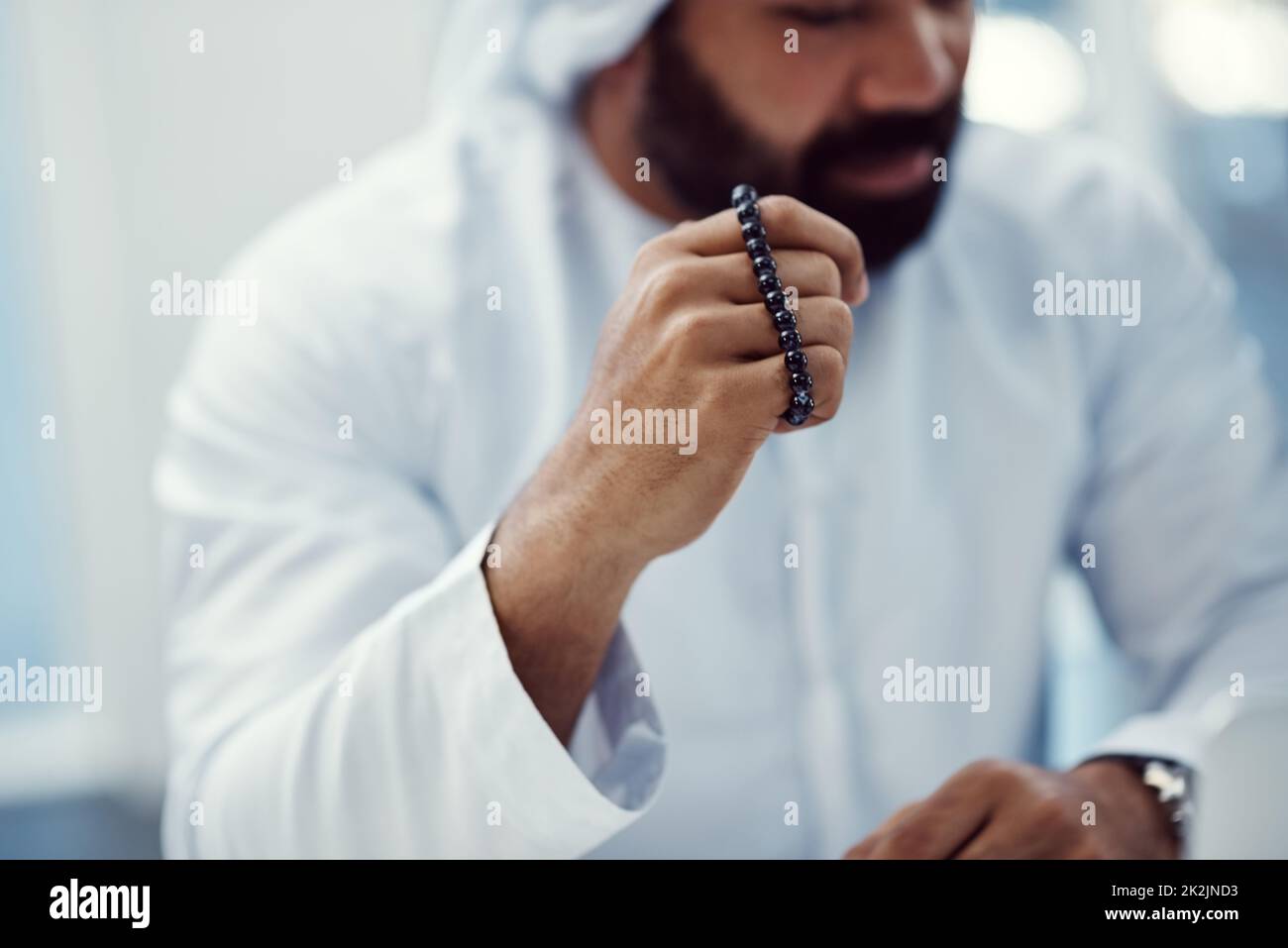 Recherche d'une intervention divine. Coupe courte d'un jeune homme d'affaires vêtu de vêtements traditionnels islamiques portant des perles de prière tout en travaillant dans son bureau. Banque D'Images