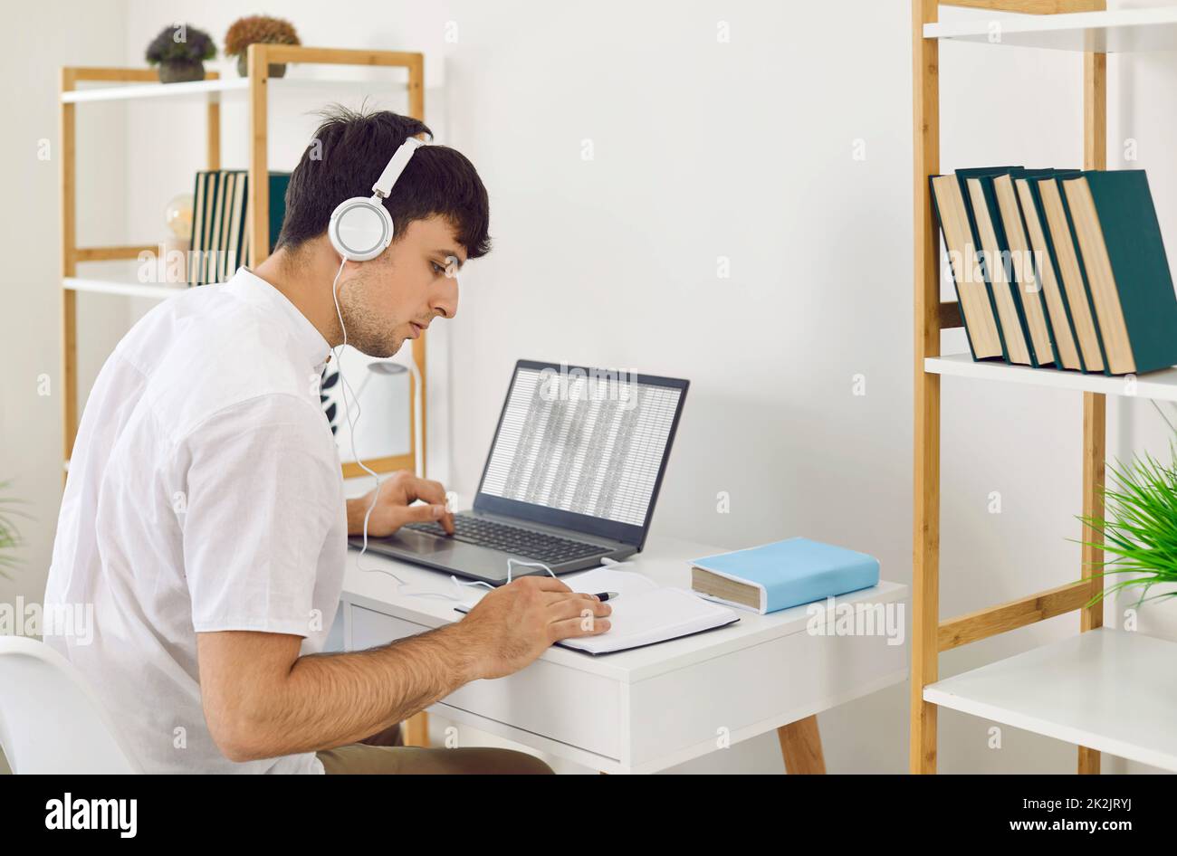 Jeune homme qui profite de la musique dans un casque et qui travaille ou étudie sur un ordinateur portable au bureau à domicile. Banque D'Images