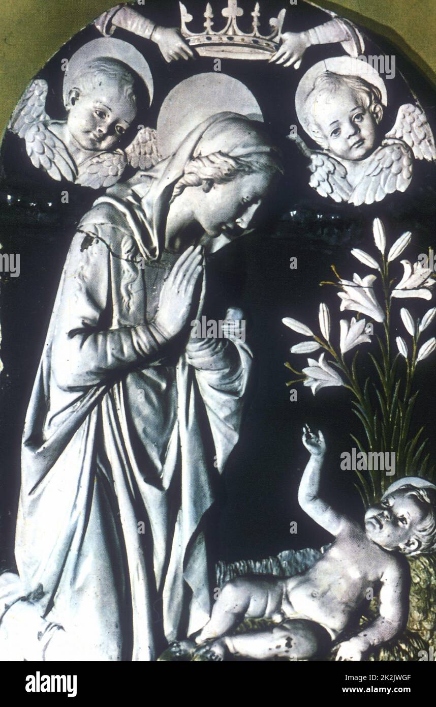 École d'Andrea Della ROBBIA (1435-1525) l'adoration. La Vierge Marie, mains en position de prière, s'agenouille au-dessus du Christ naissant. En haut, les mains tiennent la couronne de la Vierge et deux chérubins regardent vers le bas. Au centre à droite se trouvent Madonna Lilies (Cilium candidum). Terre cuite émaillée. Banque D'Images