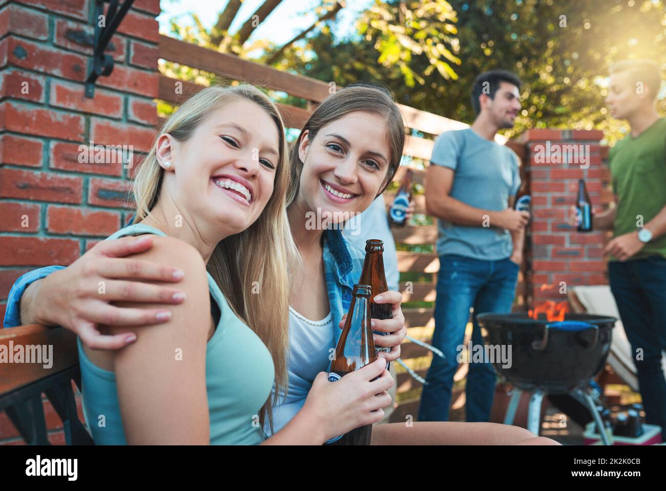 Première règle de l'été - barbecue avec des amis. Prise de deux jeunes femmes heureux appréciant des bières au barbecue avec leurs amis. Banque D'Images