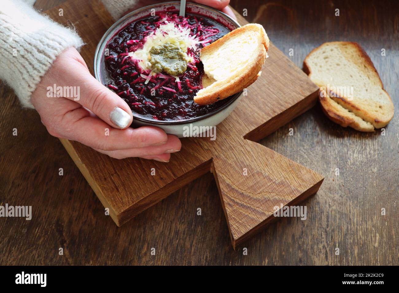 Mains de femmes tenant une assiette de soupe de légumes avec betterave, fromage, crème sure et pain sur fond de bois arustic Banque D'Images