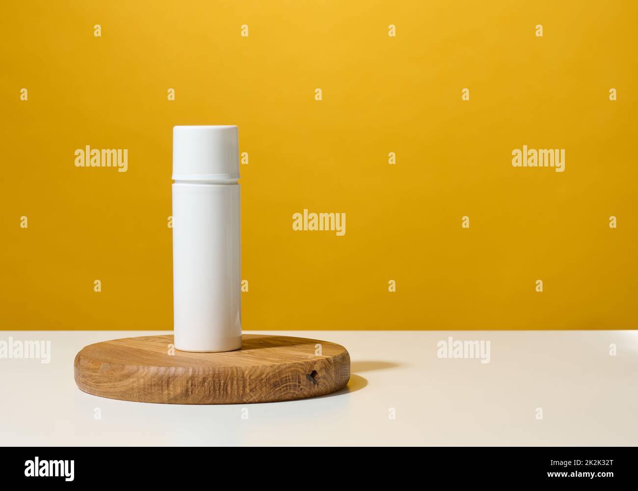 tube rond en plastique blanc pour cosmétiques, crèmes et gels liquides sur un podium en bois, fond jaune Banque D'Images