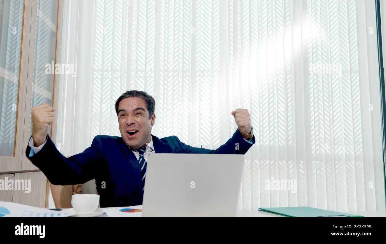 Un homme d'affaires heureux a surpris le travail au bureau blanc avec ordinateur portable de bureau de jeter des documents de compte papier Banque D'Images
