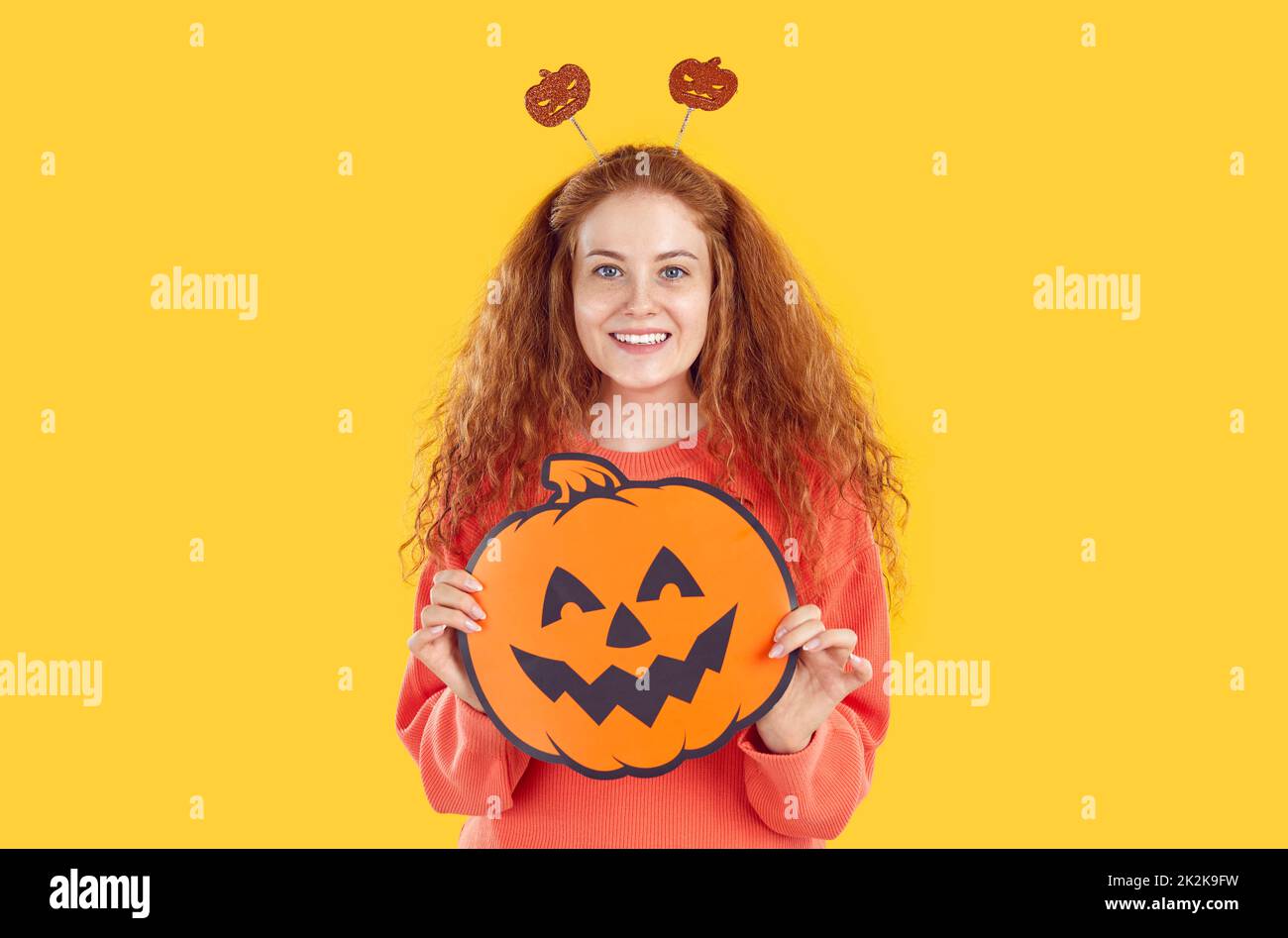 Bonne jeune femme dans les antennes de citrouille drôle tenant la citrouille d'Halloween et souriant Banque D'Images