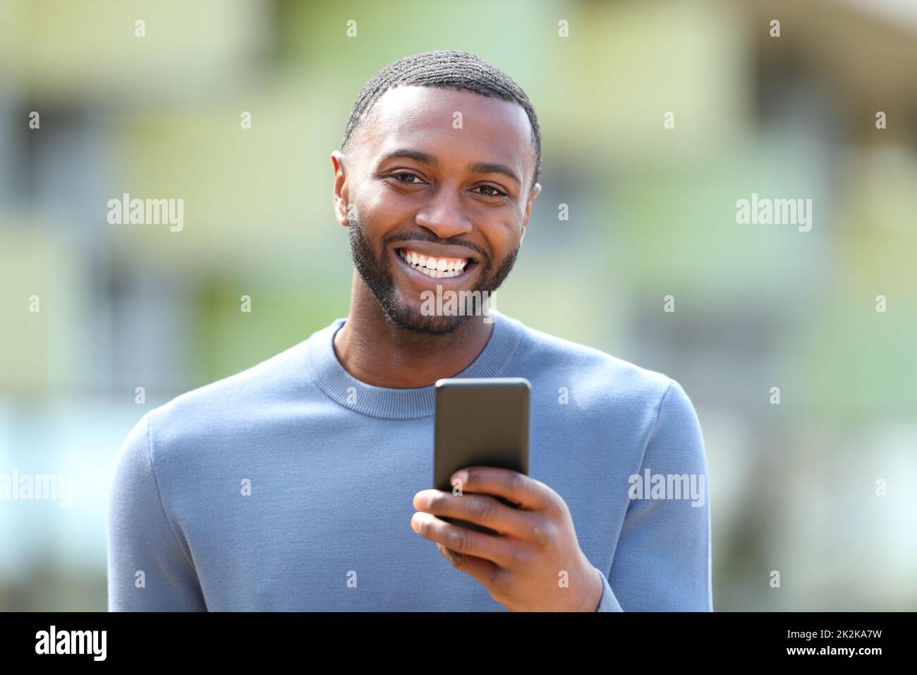 Un homme heureux avec une peau noire tient le téléphone et vous regarde Banque D'Images