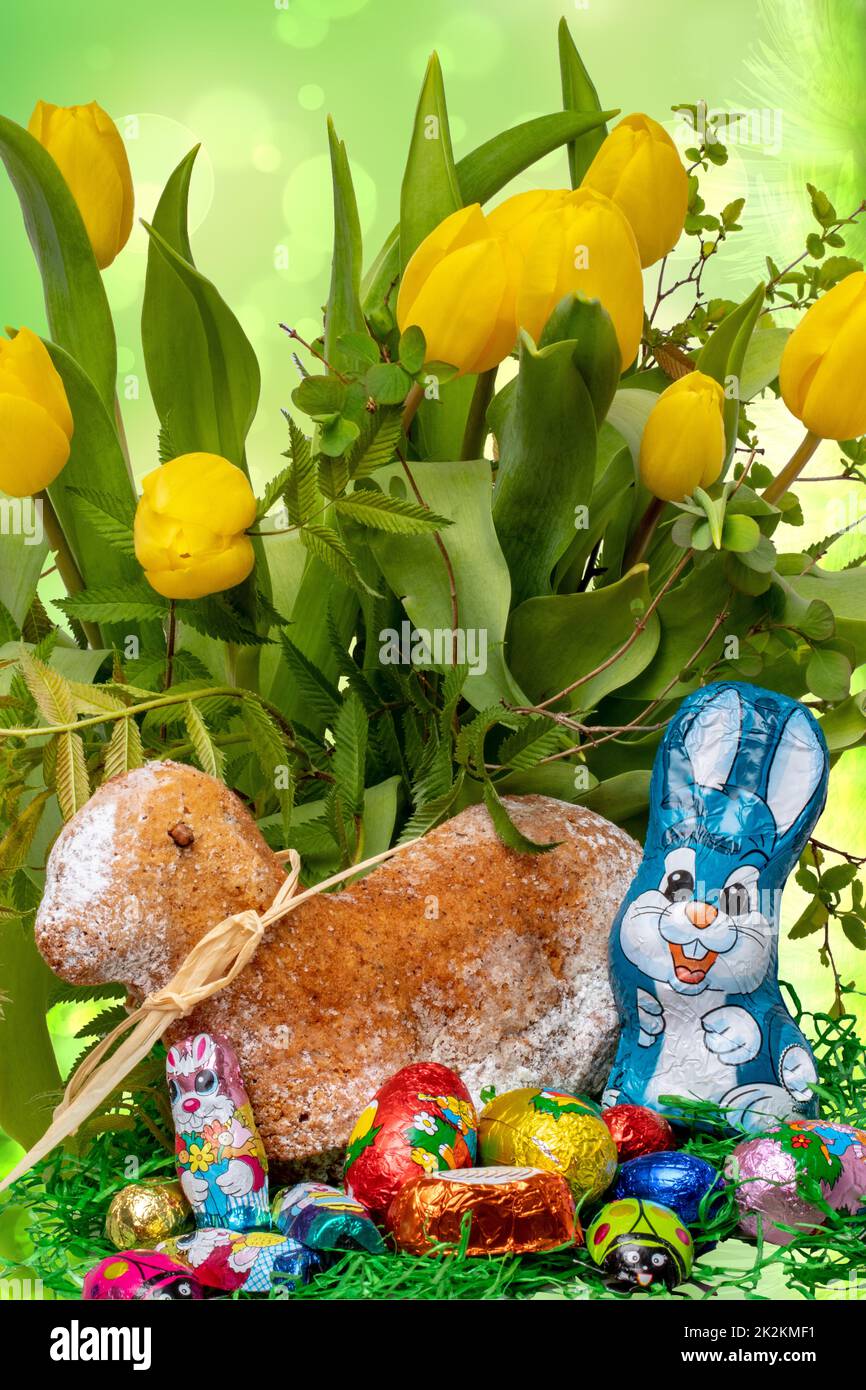 Modèle de carte de Pâques. Un gâteau traditionnel d'agneau de Pâques avec ruban et un lapin de Pâques et beaucoup d'autres bonbons au chocolat sur fond de bouquet de tulipes jaunes. Macro. Banque D'Images
