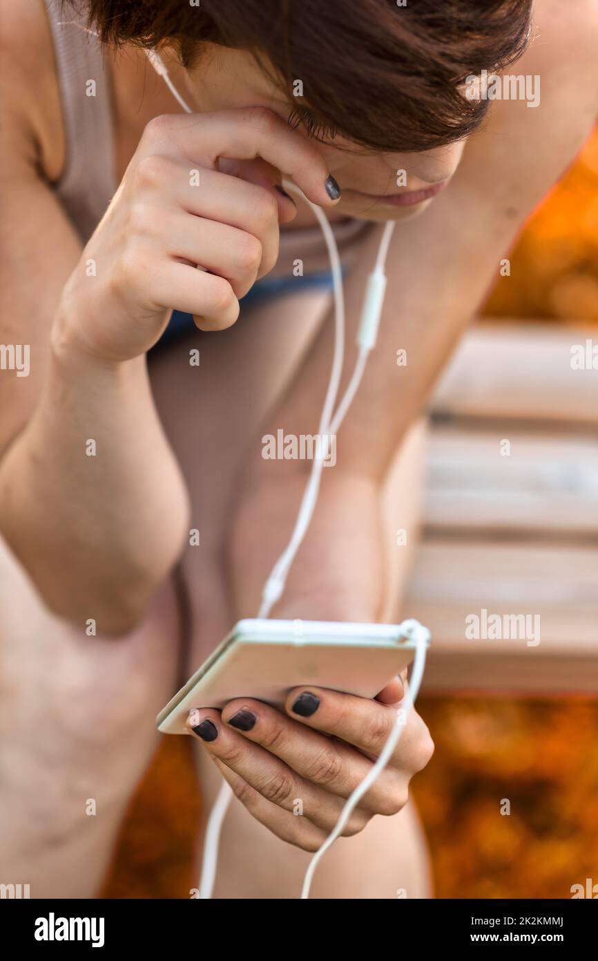 Femme assise sur un banc, penchée vers l'avant pour écouter de la musique Banque D'Images