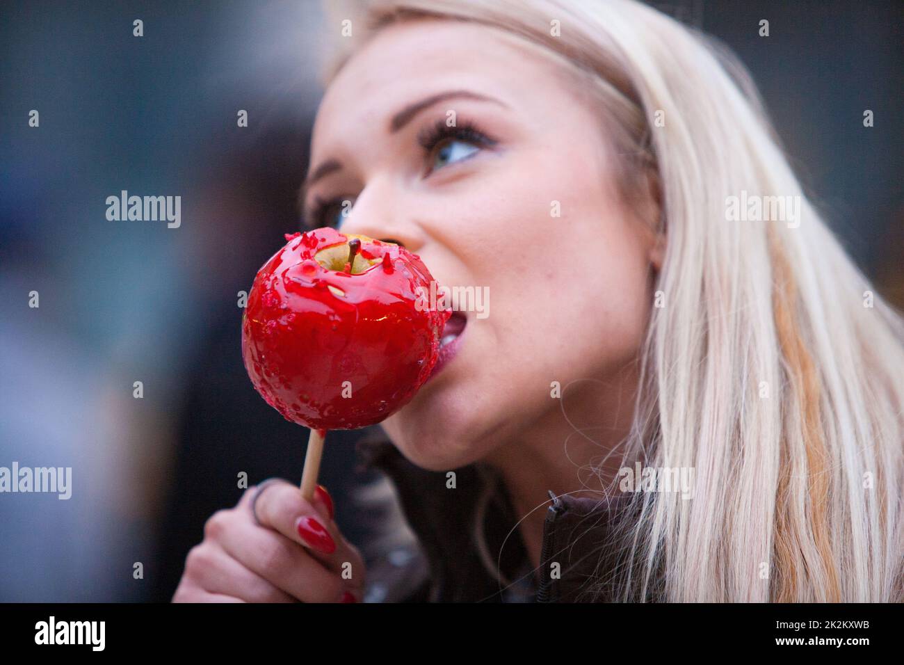 femme blonde goûtant un bonbon de pomme rouge Banque D'Images