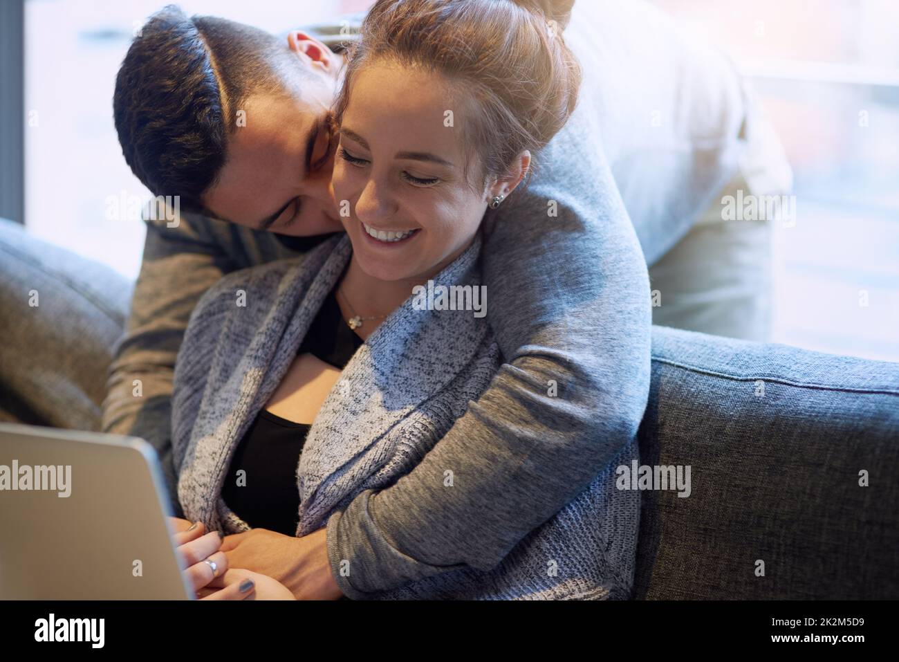 Elle la montre avec affection. Photo d'un jeune couple affectueux surfant sur le net tout en se relaxant sur le canapé à la maison. Banque D'Images