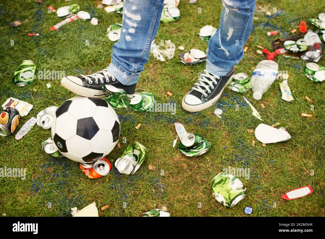 Coup de pied dans les suites. Une personne jouant avec un football au milieu des détritus laissés à un festival de musique. Banque D'Images