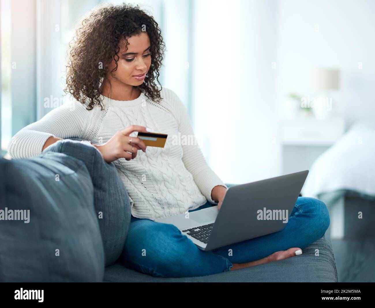 Grâce à la commodité de la technologie. Photo d'une jeune femme tenant sa carte de crédit tout en utilisant son ordinateur portable à la maison. Banque D'Images