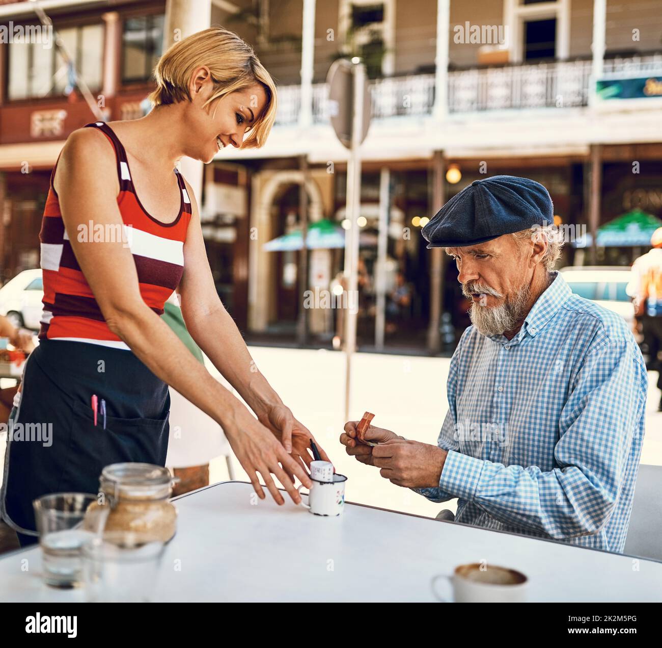 HES toujours généreux avec son bout. Photo d'une serveuse sympathique servant un homme âgé à une table devant un café. Banque D'Images