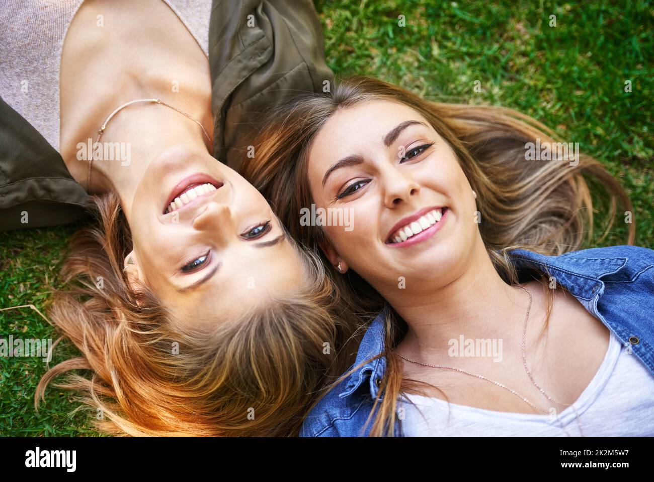 Les amis sont ce qui fait vraiment l'été. Portrait en grand angle de deux jeunes femmes attirantes qui se trouvent sur l'herbe à l'extérieur. Banque D'Images