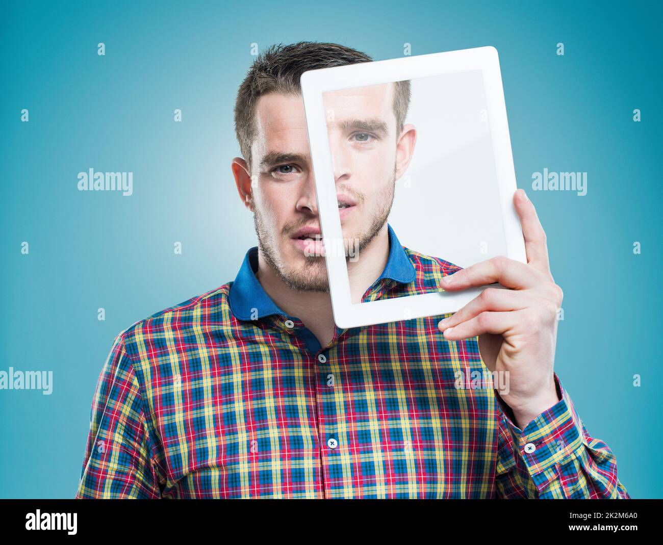 Technologie personnalisée - Une partie de l'existence quotidienne. Un jeune homme tenant une tablette numérique avancée devant son visage. Banque D'Images