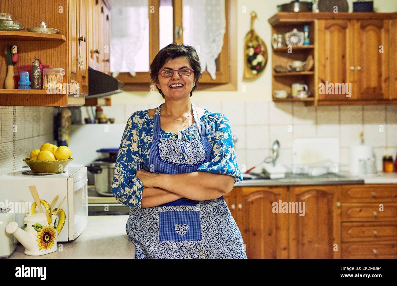 Des shes qui vont faire cuire un orage dans la cuisine. Portrait d'une femme mûre et gaie debout avec les bras repliés tout en regardant dans l'appareil photo dans la cuisine à la maison. Banque D'Images