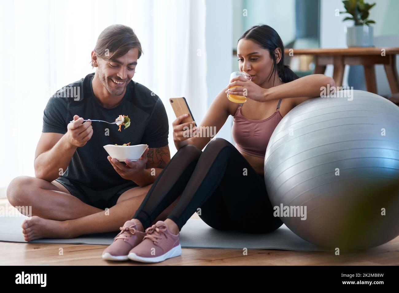 Collations après l'entraînement. Prise de vue en longueur d'un jeune couple athlétique qui profite de collations saines après son entraînement à la maison. Banque D'Images